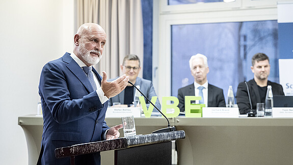 urban20251205-01-068 Ein Mann steht hinter einem Rednerpult und spricht in ein Mikrofon