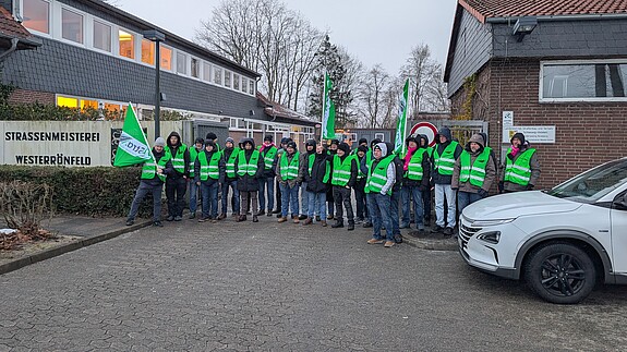 Eine Gruppe Menschen in grünen Warnwesten protestiert vor einem Gebäude
