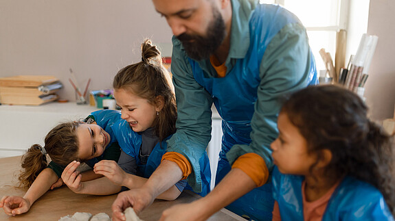 Zuwanderung und Integration Eine Gruppe kleiner Kinder arbeitet mit ihrem Lehrer im Kunstunterricht mit Ton.