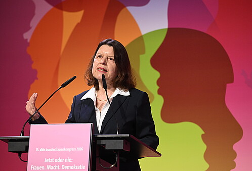 Eine Frau steht hinter einem Rednerpult und spricht in das Mikrofon
