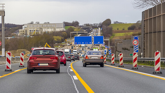 Zu sehen sind Autos auf einer Autobahn, rechts und links am Fahrbahnrand stehen Baustellen-Barken.