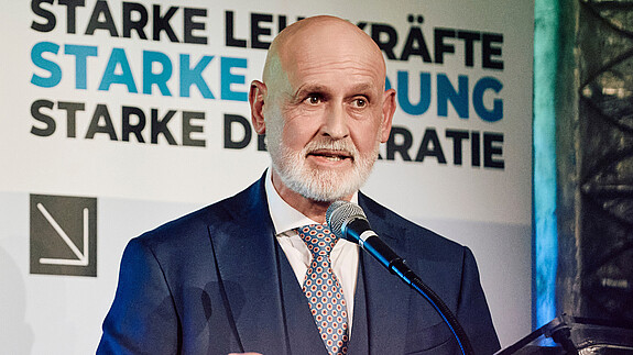 Herr Geyer steht hinter einem Rednerpult und spricht in das Mikrofon