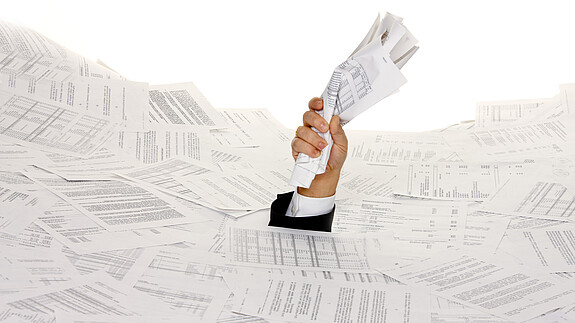 Onlinezugangsgesetz Das Foto zeigt eine Hand, die hilflos zwischen Papierbergen hervorlugt.