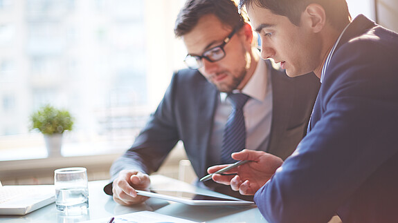 Digitalisierung Zwei Männer im Büro sehen gemeinsam auf Tablet und besprechen sich