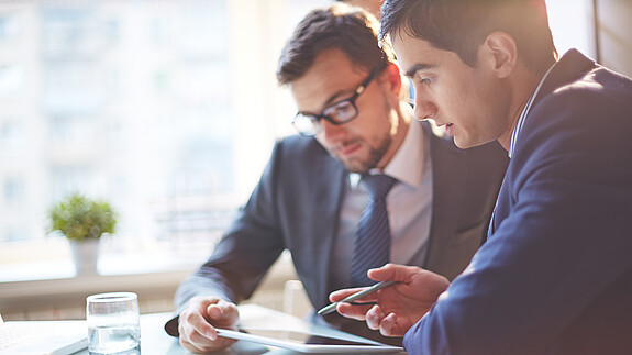 Zwei Männer im Büro sehen gemeinsam auf Tablet und besprechen sich