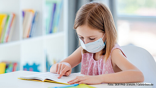 Schülerin liest Buch mit Maske in Klassenzimmer Schülerin liest Buch mit Maske in Klassenzimmer